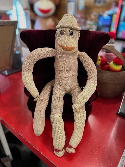 Luno, the real sock monkey: faded cream knit, a little knit hat, button eyes and an orange-red mouth, sitting in a tiny burgundy velvet armchair
